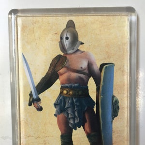 Puede incluir: Una ilustración vintage que representa a un gladiador romano, conocido como Secutor. Lleva un casco con una máscara facial, una protección de brazo de cuero, una falda corta y sandalias. Sostiene una espada en su mano derecha y un escudo en su mano izquierda. La imagen está sobre un fondo beige.