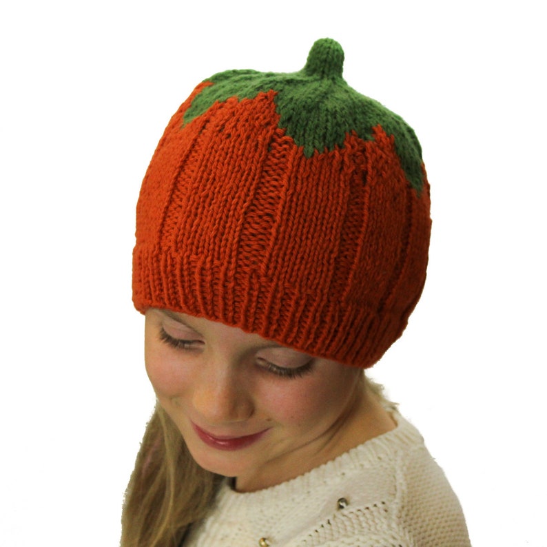 Puede incluir: Un gorro de punto de calabaza de color naranja y verde. El gorro lo lleva puesto un ni&ntilde;o con el pelo rubio.