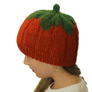 Puede incluir: Un gorro de punto de calabaza en naranja y verde. El gorro tiene una parte superior puntiaguda y una textura acanalada.