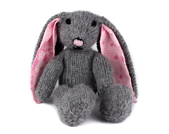 May include: A gray knitted bunny rabbit toy with pink fabric ears. The ears have a floral pattern.