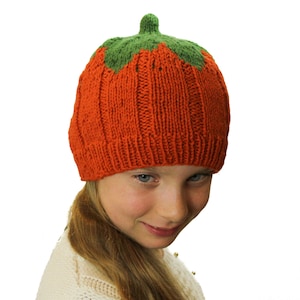 Puede incluir: Un gorro de punto naranja y verde en forma de calabaza. El gorro tiene un tallo verde en la parte superior y est&aacute; hecho con un punto de canal&eacute;.