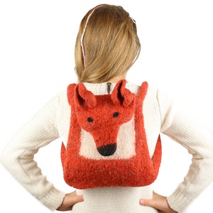 May include: A red fox-shaped backpack made of wool felt. The backpack has a zipper closure and a white felt face with black eyes and a nose.