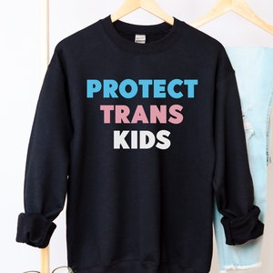 May include: Black sweatshirt with the text "PROTECT TRANS KIDS" in blue, pink, and white lettering.