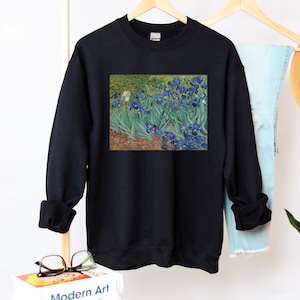 May include: Black sweatshirt with a print of a painting of blue irises on a green background.