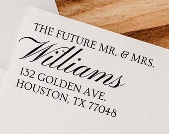 May include: White envelope with the text "THE FUTURE MR. & MRS. Williams" and address information in black. The envelope is on a wooden surface.