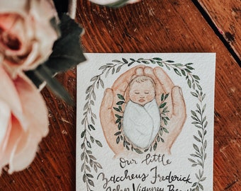 May include: Watercolor painting of a baby in a white swaddle, cradled in two hands. The baby is surrounded by a wreath of green leaves. The text reads "Our little Zaccheus Frederick John Vidunney Bezy Forever in our hearts August 4, 2022".