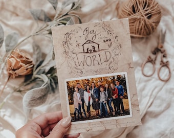 May include: A holiday card with the words "Joy to the World" and a family photo. The card has a vintage look with a beige background and decorative illustrations. The family photo is in the center of the card.