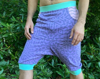 May include: Purple and teal patterned shorts with a pink and white pocket. The shorts have a wide waistband and a loose fit.