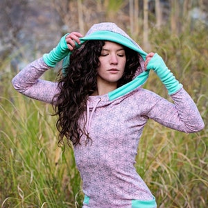 Puede incluir: Un vestido rosa con capucha con un estampado geométrico y detalles turquesa. El vestido presenta una capucha con cordón, mangas largas y largo mini falda. Las mangas y el dobladillo están ribeteados en turquesa. El vestido está hecho de un material suave y cómodo.