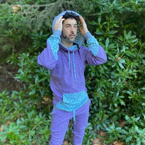 May include: A purple and blue patterned hoodie and matching sweatpants. The hoodie has a drawstring and a large hood. The sweatpants have a drawstring waistband.