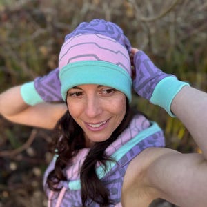 May include: A woman wearing a purple, pink, and teal patterned beanie and matching fingerless gloves. The beanie has a folded cuff.