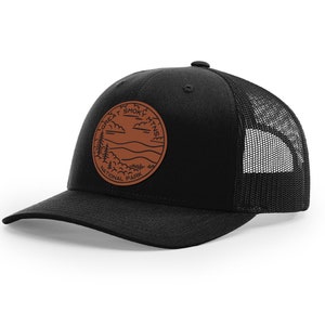 May include: Black trucker hat with a brown leather patch featuring the Great Smoky Mountains National Park logo.