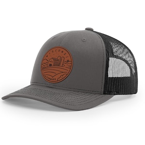 May include: A gray and black trucker hat with a brown leather patch featuring a farm scene and the text "Wisconsin Forward".