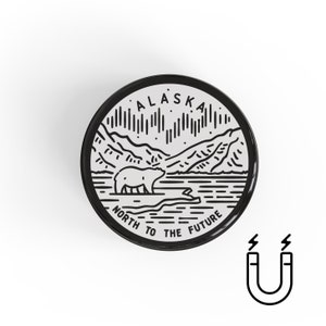May include: Black and white illustration of a polar bear walking on a snowy landscape with mountains in the background. The text "ALASKA NORTH TO THE FUTURE" is written around the image. The image is on a round, black magnet.