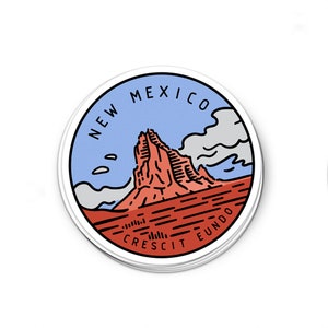 May include: A round sticker with a blue and red design. The sticker features a mountain range with the text "NEW MEXICO CRESCIT EUNDO" around the edge.
