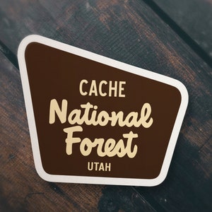 May include: A brown and white sticker with the text "CACHE National Forest UTAH" in a retro style font.