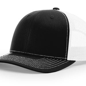 May include: A black and white trucker hat with a white mesh back. The hat has a curved brim and a white stitching detail.