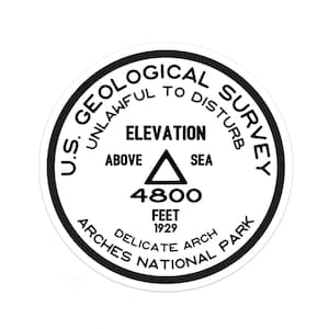 May include: A black and white round sticker with the text "U.S. GEOLOGICAL SURVEY UNLAWFUL TO DISTURB" around the edge. In the center is a triangle with the text "ELEVATION ABOVE SEA 4800 FEET 1929" and the text "DELICATE ARCH ARCHES NATIONAL PARK".