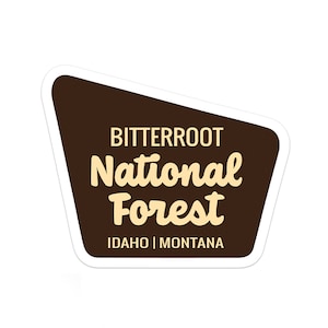 May include: A brown and white sticker with the text "Bitterroot National Forest Idaho | Montana".