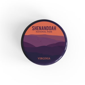 May include: A round sticker with a purple mountain range silhouette against an orange sunset. The text "Shenandoah National Park" is in black text above the mountains and "Virginia" is in black text below the mountains.