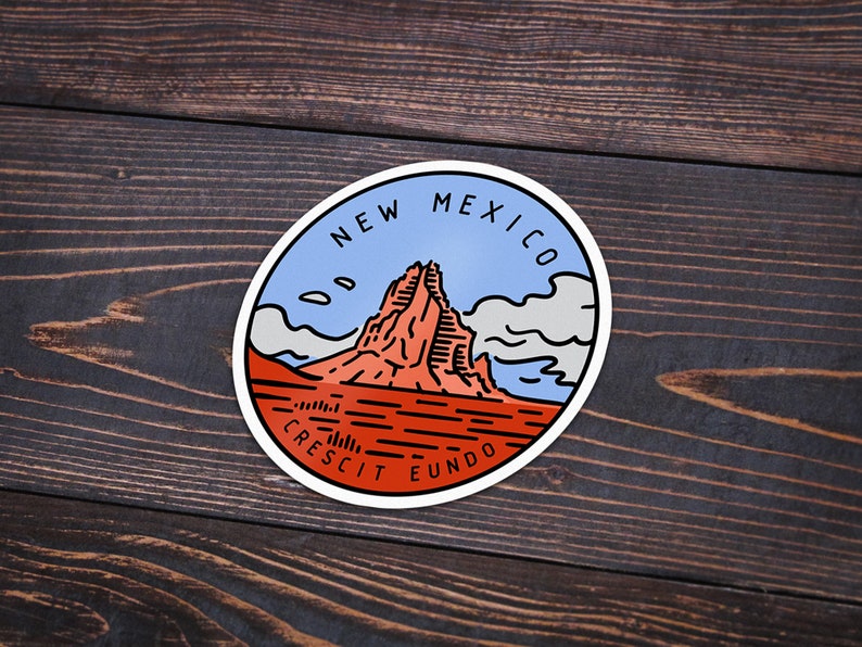 May include: A round sticker with a blue, white, and red design. It features a mountain range with the text "NEW MEXICO" and "CRESCIT EUNDO" around the edge.
