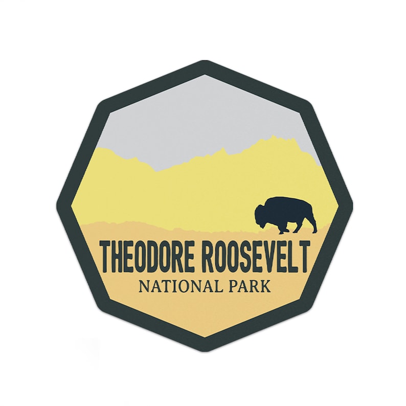May include: A yellow and gray octagon-shaped sticker with a black silhouette of a bison walking across a yellow field. The text "Theodore Roosevelt National Park" is printed in black at the bottom of the sticker.