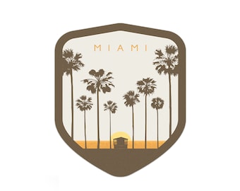 May include: A brown shield-shaped sticker with the word "MIAMI" in white text. The sticker features a silhouette of palm trees and a small building against a sunset background.
