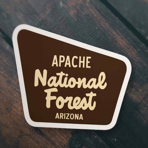 May include: A brown and white sticker with the text "APACHE National Forest ARIZONA" in a retro style font.