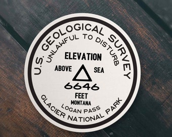 Peut inclure: Un autocollant rond blanc avec du texte noir qui dit "U.S. Geological Survey Unlawful to Disturb" et "Elevation Above Sea 6646 Feet Montana Logan Pass Glacier National Park".