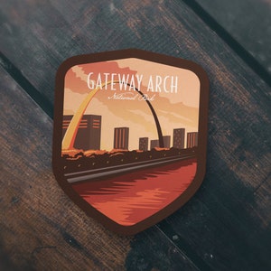 May include: A vintage-style illustrated patch featuring the Gateway Arch National Park in St. Louis, Missouri. The patch is brown with a shield shape and features a sunset scene with the iconic arch in the background. The text "GATEWAY ARCH National Park" is printed in white on the patch.