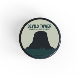 May include: A black and white illustration of Devils Tower National Monument in Wyoming. The illustration is on a round, cream-colored background with a black border.