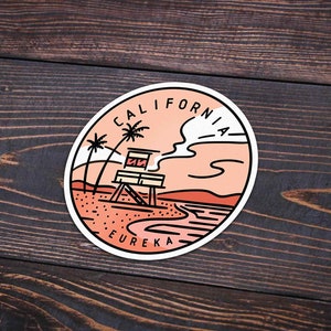 May include: A round sticker with a peach background featuring a line drawing of a lifeguard tower on a beach with palm trees and a cloud. The text "CALIFORNIA" is written in a circle around the top of the sticker and "EUREKA" is written at the bottom.