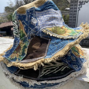 May include: A multi-coloured patchwork bucket hat with a frayed edge. The hat is made of different fabrics and patterns, including blue, brown, and white.