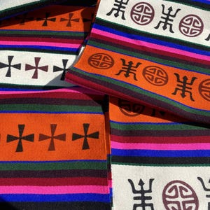 May include: Multicolored woven fabric with a repeating pattern of crosses and circles. The fabric is folded in layers, revealing different colors and patterns.