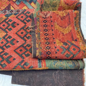 May include: Close-up of colorful fabric pieces with geometric and floral patterns. The textiles feature shades of red, orange, green, and brown. The fabric appears to be layered, showcasing various textures and designs.