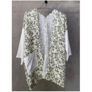 May include: A floral print kimono-style jacket with white sleeves and pocket details. The jacket features a cream-colored background with a pattern of green leaves and small yellow flowers. It hangs on a metal hanger against a neutral background.