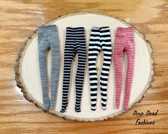 May include: Four pairs of doll-sized striped leggings in black and white, red and white, and two different shades of gray and white.