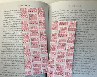 May include: Two rectangular bookmarks with the words "READ MORE BOOKS" in a repeating pattern. The text is in white on a pink background. The bookmarks are placed in an open book.