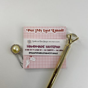 May include: A pink notepad with a grid pattern and the text "Per My Last Email" in red. The notepad is 8.7 cm by 8.7 cm and has 30 sheets. It is labelled "Handmade Notepad" and includes the text "Sparkle and Shine Designs hand drawn stickers" and "@ShopSparkleShineStudios". A gold pen with a diamond-shaped top is next to the notepad. A silver paper clip with a pearl-like embellishment is on the notepad.