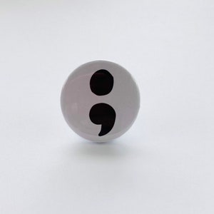 May include: A white button with a black semicolon symbol.