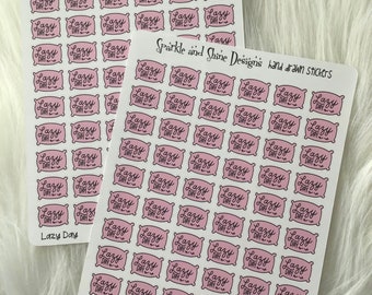 May include: A sheet of pink and white stickers with the text "Lazy Day" in a cursive font. The stickers are shaped like pillows and are arranged in a grid pattern. The text "Sparkle and Shine Designs hand drawn stickers" appears at the top of the sheet.