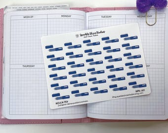 May include: A sheet of white stickers with blue insulin pen illustrations, placed on an open planner. The planner has a pink cover and grid-lined pages. The stickers are labeled "INSULIN PEN" and "Sparkle Shine Studios."