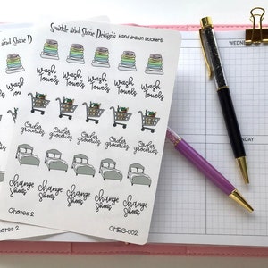 May include: A set of three sheets of stickers featuring hand-drawn illustrations of household chores. The stickers include images of laundry, groceries, and changing sheets. The stickers are printed on white paper with black ink.