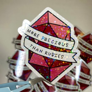 May include: A holographic sticker with a red gem design and the text "More Precious Than Rubies".