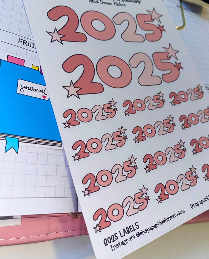 May include: A sheet of stickers with the year 2025 printed in pink and white with a star next to each number. The stickers are on a white background and the text "2025 LABELS" is printed at the bottom of the sheet.