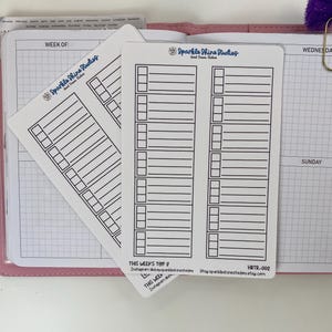 May include: White planner stickers with black lines and boxes for weekly planning. The stickers have the text "Sparkle Shine Studios" and "THIS WEEK'S TOP 2". The stickers are on a pink planner.