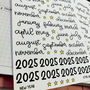 May include: A sheet of white sticker paper with black handwritten text and yellow star stickers. The stickers include the months of the year and the year 2025. The text "NEW YEAR" is also included on the sheet.