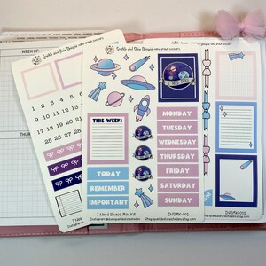 May include: A set of space-themed stickers for a planner or journal. The stickers feature planets, stars, rockets, and a UFO. The stickers are in shades of blue, purple, and pink. The stickers are labeled "I Need Space" and "This Week".