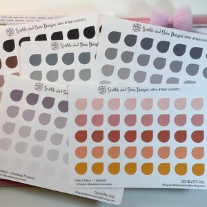 May include: A set of 6 sheets of hand-drawn sticker designs featuring various shades of grey, purple, pink, brown, and gold. Each sheet has 36 stickers in the shape of a teardrop. The sheets are labelled "Dew Drops" and include the names of each colour scheme: "Smokey Mauves", "Harvest", and "Golden Sunset".