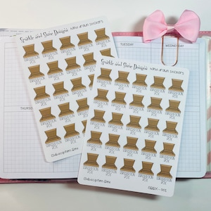 May include: Two sheets of stickers with brown subscription box illustrations. The stickers are labeled "Subscription Box" in black text. The text "Sparkle and Shine Designs hand drawn stickers" is also visible. A pink bow and a pen are also in the image.